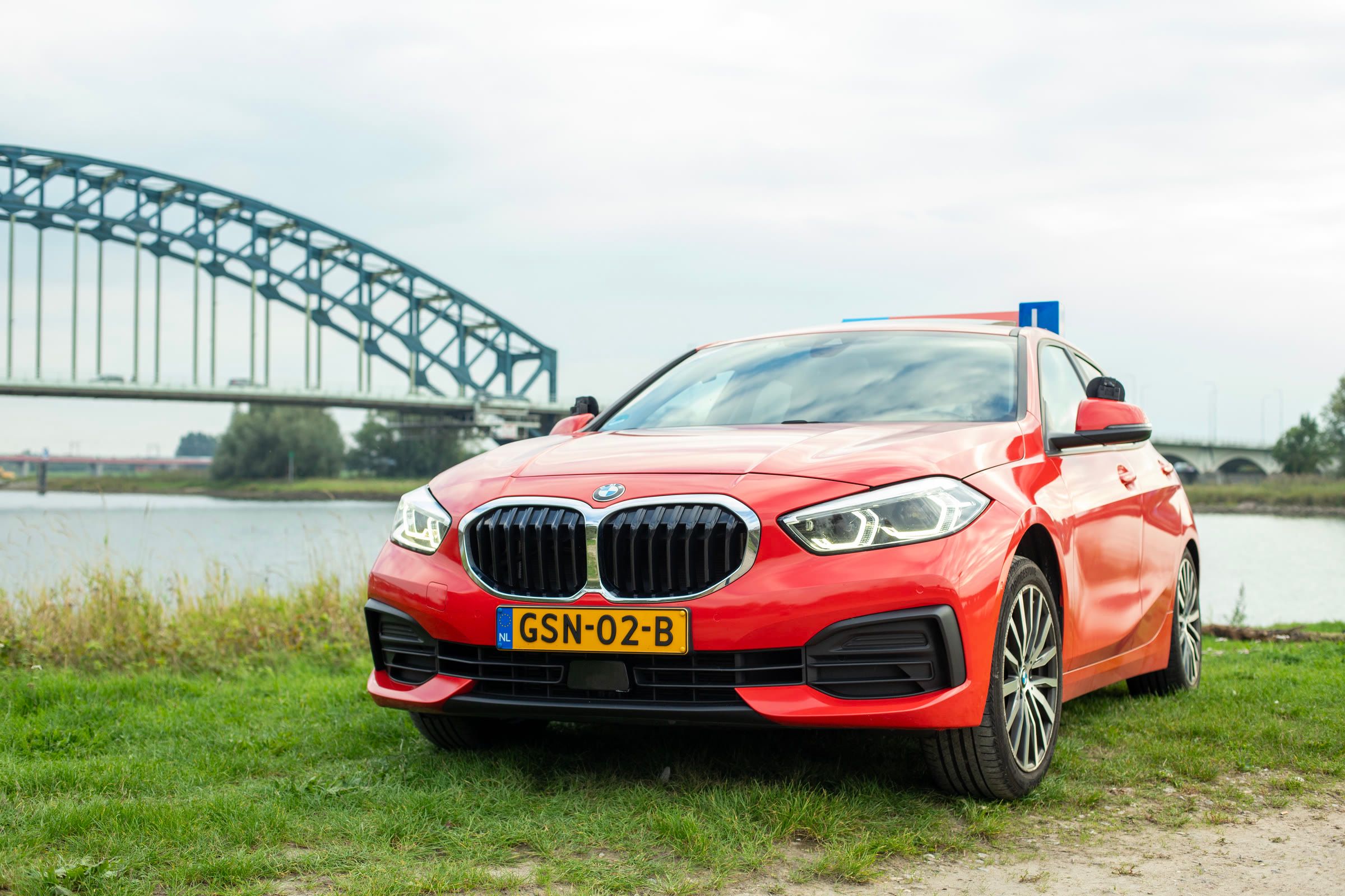 Rode BMW 118d van ROadwise met lesbord op het dak, geparkeerd aan de rivier